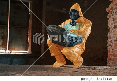 Case with blue glowing light. Hazard materials. Man dressed in chemical protection suit in the ruins of the post apocalyptic building 125144361