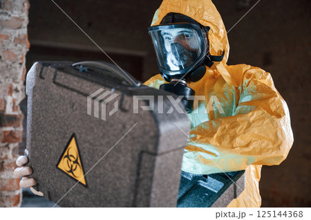 Frightened scientist is with radioactive materials. Man dressed in chemical protection suit in the ruins of the post apocalyptic building 125144368