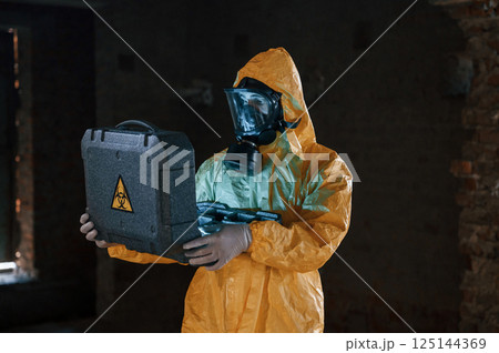 Frightened scientist is with radioactive materials. Man dressed in chemical protection suit in the ruins of the post apocalyptic building 125144369