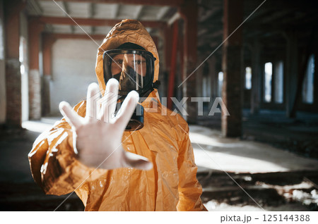 Stop sign by hand. Man dressed in chemical protection suit in the ruins of the post apocalyptic building 125144388