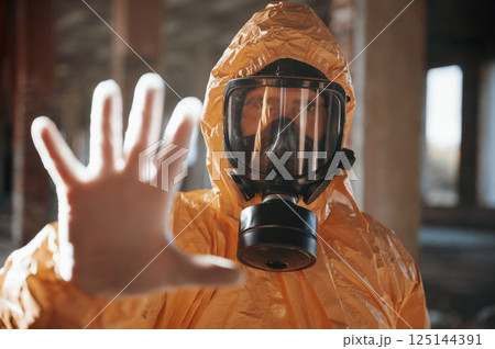 Stop sign by hand. Man dressed in chemical protection suit in the ruins of the post apocalyptic building Stop sign by hand. Man dressed in chemical protection suit in the ruins of the post apocalyptic building 125144391