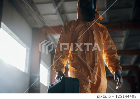 Walking with hard case. Man dressed in chemical protection suit in the ruins of the post apocalyptic building Walking with hard case. Man dressed in chemical protection suit in the ruins of the post apocalyptic building 125144408