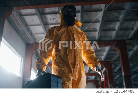 Walking with hard case. Man dressed in chemical protection suit in the ruins of the post apocalyptic building Walking with hard case. Man dressed in chemical protection suit in the ruins of the post apocalyptic building 125144409