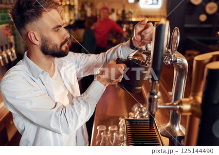 Side view. Bartender pours beer. Man is working in the bar Side view. Bartender pours beer. Man is working in the bar 125144490