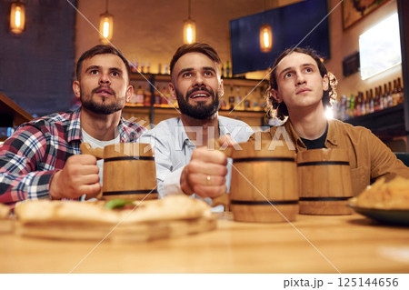 Watching TV. Three friends are in the bar drinking beer and having a good time 125144656