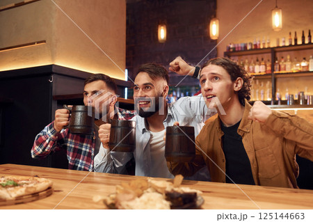 Soccer fans watching match. Three friends are in the bar drinking beer and having a good time Soccer fans watching match. Three friends are in the bar drinking beer and having a good time 125144663