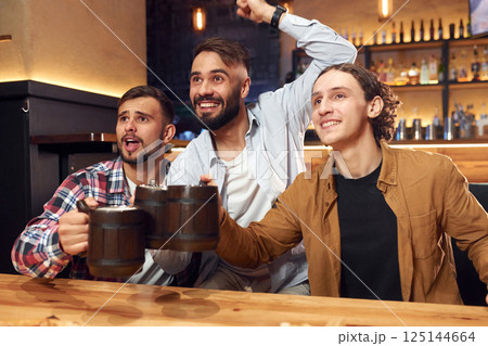 Soccer fans watching match. Three friends are in the bar drinking beer and having a good time Soccer fans watching match. Three friends are in the bar drinking beer and having a good time 125144664