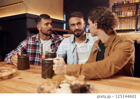 Having a conversation. Three friends are in the bar drinking beer and having a good time Having a conversation. Three friends are in the bar drinking beer and having a good time 125144681