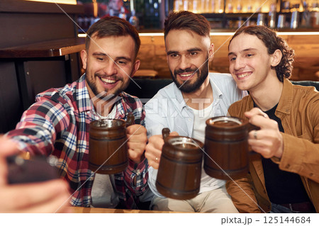 Making selfie. Three friends are in the bar drinking beer and having a good time Making selfie. Three friends are in the bar drinking beer and having a good time 125144684