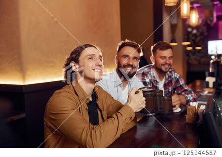 Sitting and smiling. Three friends are in the bar drinking beer and having a good time Sitting and smiling. Three friends are in the bar drinking beer and having a good time 125144687