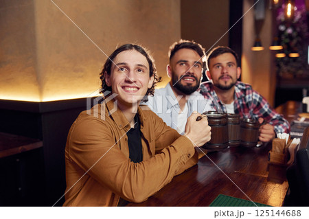 Sitting and smiling. Three friends are in the bar drinking beer and having a good time 125144688