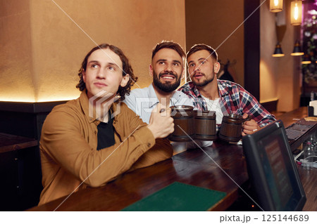 Sitting and smiling. Three friends are in the bar drinking beer and having a good time Sitting and smiling. Three friends are in the bar drinking beer and having a good time 125144689