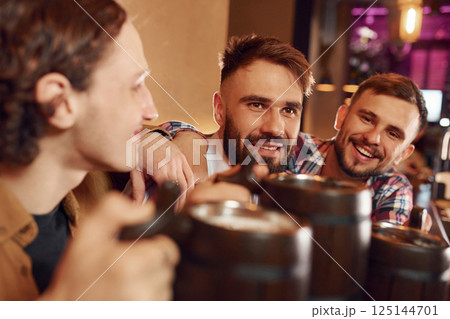Sitting by the table. Three friends are in the bar drinking beer and having a good time Sitting by the table. Three friends are in the bar drinking beer and having a good time 125144701