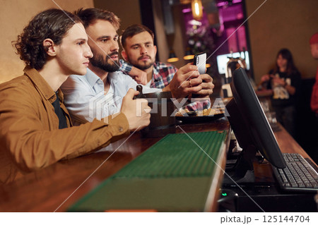 Sitting by the table. Three friends are in the bar drinking beer and having a good time Sitting by the table. Three friends are in the bar drinking beer and having a good time 125144704
