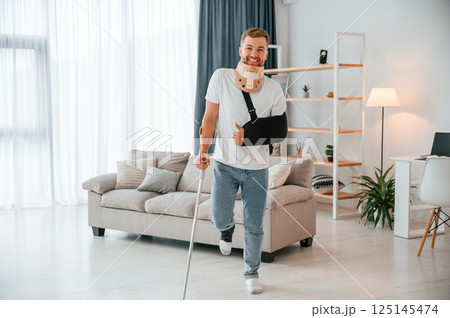 Standing and smiling. Man with crutches is at home indoors. Having injuries 125145474