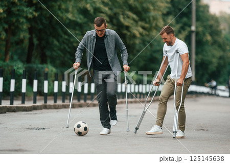 Playing soccer. Two men with crutches is outdoors on the road 125145638