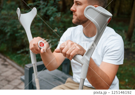 Sitting with crutches. Man is in the park outdoors. Having leg injury 125146192