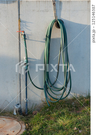 Coiled green garden hose neatly hung on a wall next to a water tap, illustrating practical outdoor storage and efficient watering solutions for greenery and garden maintenance Coiled green garden hose neatly hung on a wall next to a water tap, illustrating practical outdoor storage and efficient watering solutions for greenery and garden maintenance 125146387