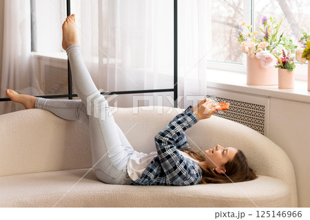 Teenage girl lying on sofa using smartphone at home. Teenage girl lying on sofa using smartphone at home. 125146966