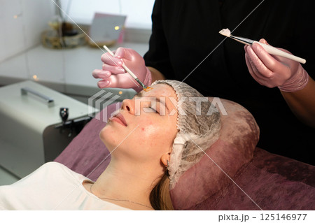 Professional applies rejuvenating face mask to client's forehead Professional applies rejuvenating face mask to client's forehead 125146977