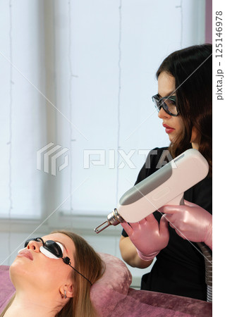Esthetician adjusts handheld laser above client's eyebrow for removal Esthetician adjusts handheld laser above client's eyebrow for removal 125146978