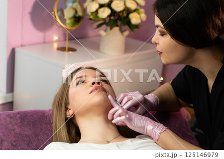 Specialist administers dermal chin filler in floral spa room 125146979