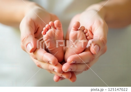 Newborn baby feet gently cradled in the hands of a caring adult in a soft, serene setting 125147022