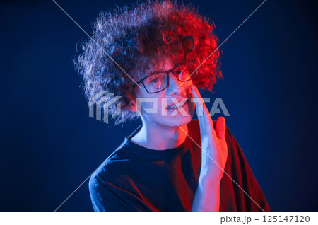 Conception of gossip. Telling a secret. Young man with curly hair is indoors illuminated by neon lighting 125147120