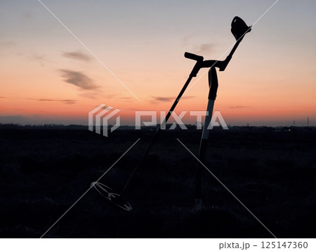 Silhouette of a metal detector and a shovel at sunset. Metal detector at the evening field. Silhouette of a metal detector and a shovel at sunset. Metal detector at the evening field. 125147360