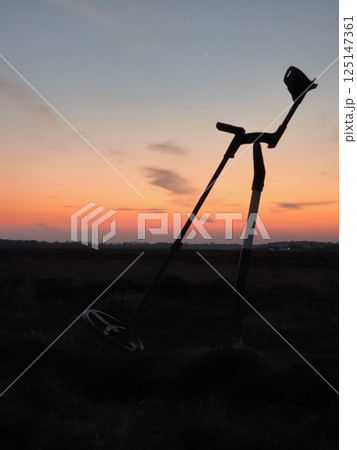 Silhouette of a metal detector and a shovel at sunset. Metal detector at the evening field. Silhouette of a metal detector and a shovel at sunset. Metal detector at the evening field. 125147361