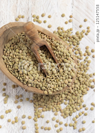 Bowl full of dried raw green lentils with a wooden scoop on white table top view. Vegetarian food Bowl full of dried raw green lentils with a wooden scoop on white table top view. Vegetarian food 125147558