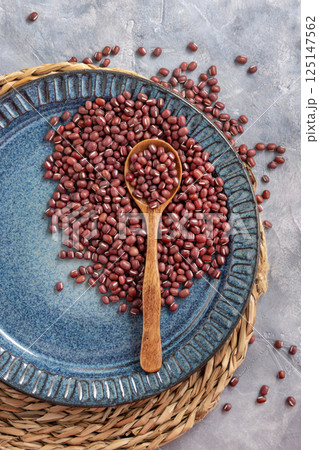 Blue plate full of dried red azuki beans with a wooden spoon top view. Vegetarian protein source 125147562