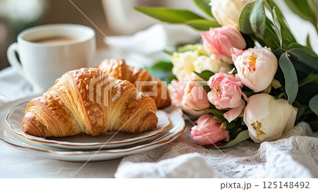 breakfast scene with two golden croissants on elegant plates, a cup of coffee, and a bouquet of soft pink and white flowers breakfast scene with two golden croissants on elegant plates, a cup of coffee, and a bouquet of soft pink and white flowers 125148492
