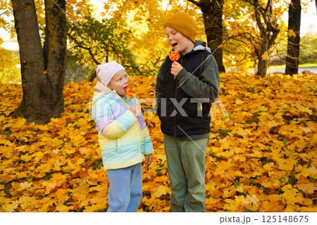 Portrait of a boy and a girl eating lollipops in an autumn park. Portrait of a boy and a girl eating lollipops in an autumn park. 125148675