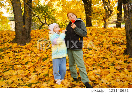 Portrait of a boy and a girl eating lollipops in an autumn park. Portrait of a boy and a girl eating lollipops in an autumn park. 125148681