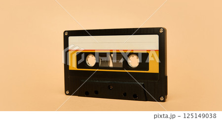 Black audio cassette tape with yellow and white label against pale beige background, evoking retro music concept Black audio cassette tape with yellow and white label against pale beige background, evoking retro music concept 125149038