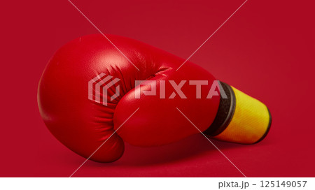 Single, vibrant red boxing glove with yellow and black wrist wrap against matching deep red background. Single, vibrant red boxing glove with yellow and black wrist wrap against matching deep red background. 125149057