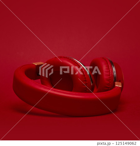 Red padded headphones with glossy accents lying on red background in pop-art style. Concept of aesthetics, vintage, pop art, design Red padded headphones with glossy accents lying on red background in pop-art style. Concept of aesthetics, vintage, pop art, design 125149062