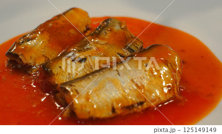 a close-up side angle of sardines in tomato sauce, showcasing the glossy texture and rich color of the fish and sauce. great for use in food packaging, recipe blogs, or advertisements related to 125149149