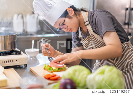 Smiling Young Female Chef Preparing a Sandwich in a Professional Kitchen 125149297