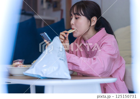 スマホを見ながらお菓子を食べる女性 125150731