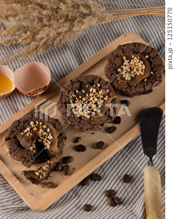 Three brown muffins on wooden tray, eggshell, butter knife, decorative reed and coffee beans on striped fabric, top view, vertical image. 125150770