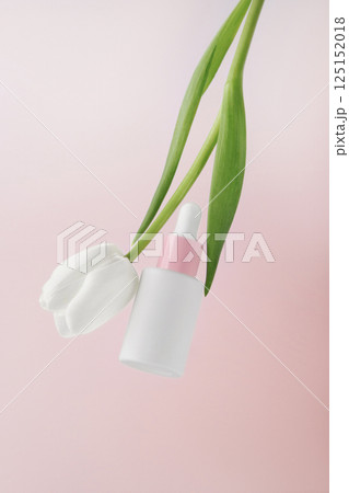 Place for text. White serum bottle. Cosmetics on a pink background. In the frame is a white flower, a tulip. Elegantly. 125152018