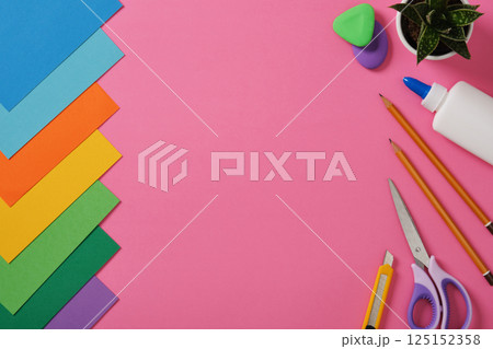 Supplies for paper art hobby: scissors, craft knife, pencil, eraser, colored paper on pink background. Space for your text. Paper crafts work table flatlay. Supplies for paper art hobby: scissors, craft knife, pencil, eraser, colored paper on pink background. Space for your text. Paper crafts work table flatlay. 125152358