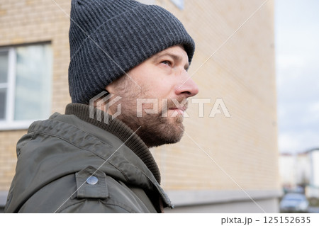 Handsome man wearing warm jacket and wool hat walking down on the city with mobile phone in hand. Stylish bearded middle-aged male using smartphone at urban street. Businessman going on job. Handsome man wearing warm jacket and wool hat walking down on the city with mobile phone in hand. Stylish bearded middle-aged male using smartphone at urban street. Businessman going on job. 125152635