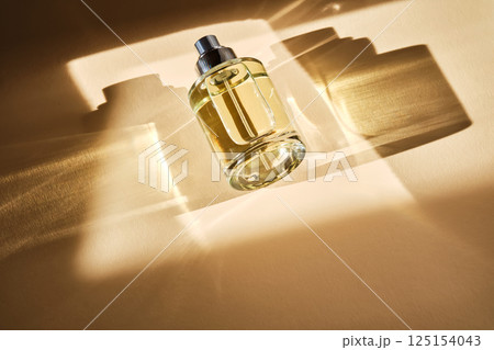 Perfume on a beige background in the rays of bright sun with beautiful highlights. 125154043