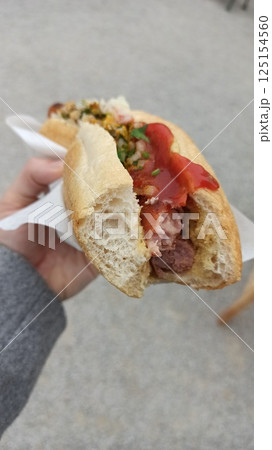 A hand holding a half-eaten hot dog with ketchup 125154560