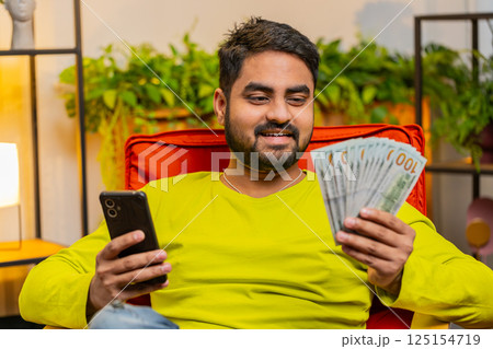 Rich happy Indian man counting money cash on smartphone calculator app, calculate income earnings 125154719