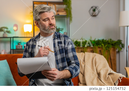 Mature man with documents analyzing information reading business papers prepare financial report Mature man with documents analyzing information reading business papers prepare financial report 125154732