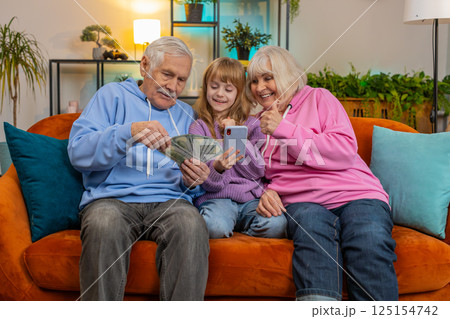 Child girl granddaughter with grandparents counting money using smartphone calculator at home Child girl granddaughter with grandparents counting money using smartphone calculator at home 125154742